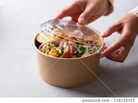 Close up of hands closing an eco-friendly paper bowl of Thai food (Pad See Ew) 136254755