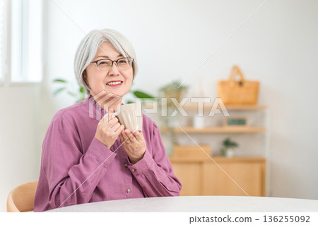 Silver-haired senior woman drinking a hot drink at the dining table at home Silver-haired senior woman drinking a hot drink at the dining table at home 136255092