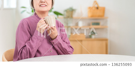 Silver-haired senior woman drinking a hot drink at the dining table at home Silver-haired senior woman drinking a hot drink at the dining table at home 136255093