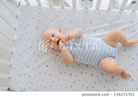 Baby lying peacefully in a cozy crib at home, feeling safe and calm in a warm nursery atmosphere. Simple everyday moment of care and comfort. Infant sleep, early childhood and gentle parenting concept Baby lying peacefully in a cozy crib at home, feeling safe and calm in a warm nursery atmosphere. Simple everyday moment of care and comfort. Infant sleep, early childhood and gentle parenting concept 136255761