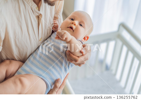 Father gently placing his baby into a crib at home, creating a calm and safe bedtime moment. Caring fatherhood scene filled with trust and warmth. Parenting, infant sleep and family bonding concept Father gently placing his baby into a crib at home, creating a calm and safe bedtime moment. Caring fatherhood scene filled with trust and warmth. Parenting, infant sleep and family bonding concept 136255762