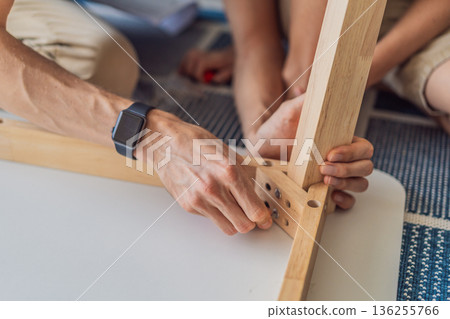 Father and his son assembling a table together in the living room at home. Meaningful family moment showing teamwork, learning and support. Fatherhood, home improvement and bonding through shared Father and his son assembling a table together in the living room at home. Meaningful family moment showing teamwork, learning and support. Fatherhood, home improvement and bonding through shared 136255766