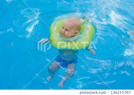 Baby swimming independently in a pool wearing a neck float ring, enjoying water safely and calmly. Cute early learning moment showing confidence and freedom. Infant swimming, water safety and healthy Baby swimming independently in a pool wearing a neck float ring, enjoying water safely and calmly. Cute early learning moment showing confidence and freedom. Infant swimming, water safety and healthy 136255767
