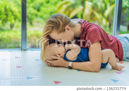 Mother and baby lying on a soft play mat at home, playing, talking and sharing a joyful moment together. Authentic family lifestyle, early childhood development and emotional bonding. Parenting and Mother and baby lying on a soft play mat at home, playing, talking and sharing a joyful moment together. Authentic family lifestyle, early childhood development and emotional bonding. Parenting and 136255774
