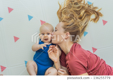 Mother and baby lying on a soft play mat at home, playing, talking and sharing a joyful moment together. Authentic family lifestyle, early childhood development and emotional bonding. Parenting and 136255779
