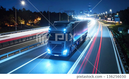 Fast cars drive with blurred motion along the dark urban highway at night, creating a cityscape of light and speed on the busy transport motorway 136256030