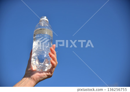 Senior's hand holding a plastic bottle of water against the blue sky Senior's hand holding a plastic bottle of water against the blue sky 136256755