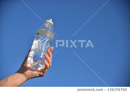 老人的手拿著一瓶塑膠水,映襯著藍天。 老人的手拿著一瓶塑膠水,映襯著藍天。 136256760