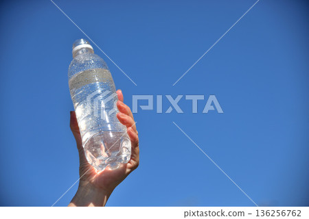 老人的手拿著一瓶塑膠水,映襯著藍天。 老人的手拿著一瓶塑膠水,映襯著藍天。 136256762