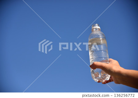 Senior's hand holding a plastic bottle of water against the blue sky 136256772
