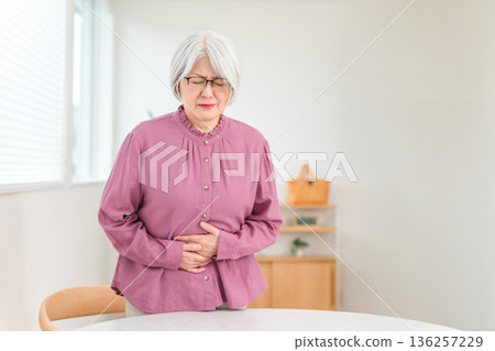 一位頭髮花白的老婦人面露痛苦之色，摀著肚子，顯然是胃痛。 136257229