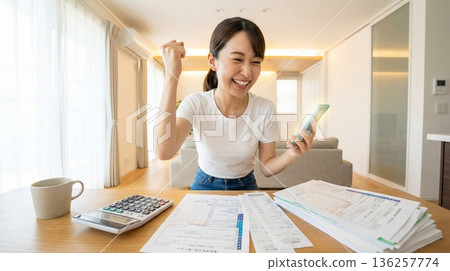 A young Japanese woman smilingly uses her smartphone at home to file her tax return. Pointing pose and household finance management image 136257774