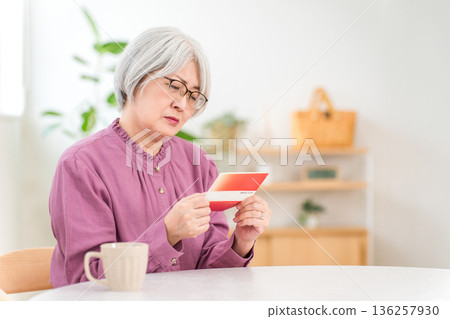 A gray-haired senior woman is troubled by her savings account book (retirement funds, savings, pension, living expenses) A gray-haired senior woman is troubled by her savings account book (retirement funds, savings, pension, living expenses) 136257930