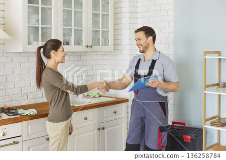 Repairman in uniform shaking hands with woman after successful repair standing in kitchen 136258784