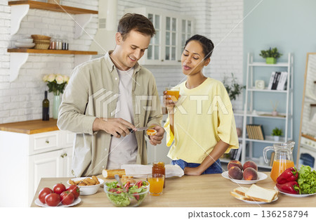 Couple preparing toast with jam and drinking juice together in bright kitchen Couple preparing toast with jam and drinking juice together in bright kitchen 136258794