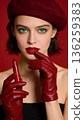 A woman in a red hat and red gloves holding a red lipstick 136259383