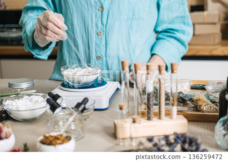 Hands in gloves use glass rod to stir powder base in bowl on scale. Fresh mixing, powder base, liquid activator, zero preservative. 136259472