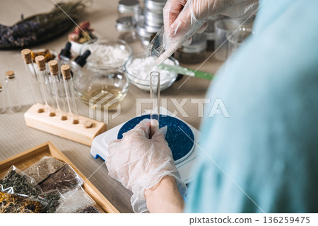 Hands in gloves pour powder from plastic bag into glass test tube on digital scale in apothecary workshop. active dry powder, zero-preservative DIY, anhydrous shelf-life, pure botanical mix. 136259475