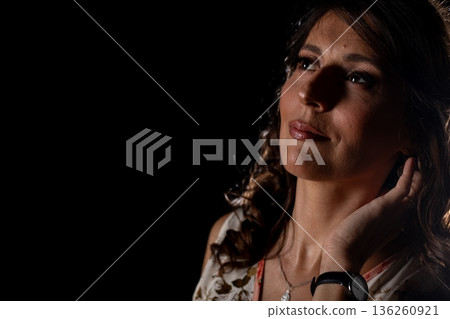 Studio shot capturing moody lighting and glossy skin texture of woman, Cinematic style image showcasing woman touching her neck with reflective expression and water accents 136260921
