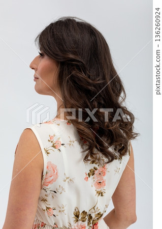 Serene female figure with floral attire and reflective mood, Graceful female profile dressed in flowers against soft studio background for versatile promotional purposes 136260924