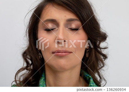 Tranquil woman with closed eyes in soft studio lighting showcasing natural look, Serene female figure with gentle makeup and peaceful demeanor captured in studio setting 136260934