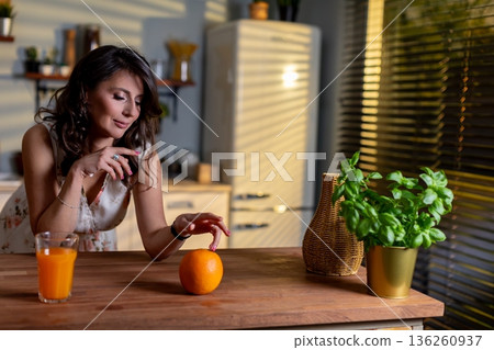 Caucasian woman reaching orange on table with thoughtful gesture, closeup of hand and fruit against warm kitchen background, moment of mindful eating and intentional selection Caucasian woman reaching orange on table with thoughtful gesture, closeup of hand and fruit against warm kitchen background, moment of mindful eating and intentional selection 136260937