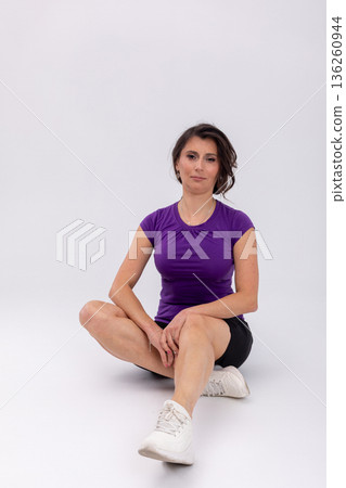 Seated woman on studio floor cooling one knee bent, relaxed expression, posttraining stretch, white sneakers, black shorts, recovery routine, mindful breathing, balanced wellness Seated woman on studio floor cooling one knee bent, relaxed expression, posttraining stretch, white sneakers, black shorts, recovery routine, mindful breathing, balanced wellness 136260944