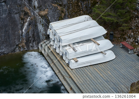 Stack of rental boats on a wooden dock next to a half-frozen lake, showcasing off-season recreation and cold weather activity. 136261004
