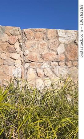 Serene Rural Landscape With Stones. Sunlit Rustic Wall Surrounded By Lush Grasses. Bright Rural Setting Featuring Ancient Stones And Wild Grasses Under Clear Blue Sky Serene Rural Landscape With Stones. Sunlit Rustic Wall Surrounded By Lush Grasses. Bright Rural Setting Featuring Ancient Stones And Wild Grasses Under Clear Blue Sky 136262268