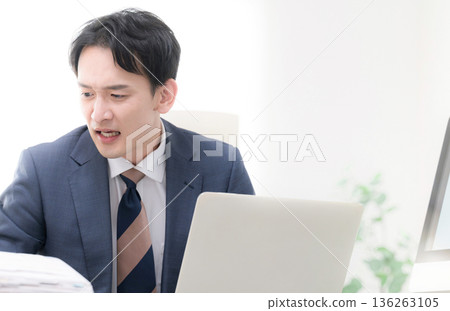 畫面中，一位身著西裝的男士，神情焦慮、心事重重、忙碌不堪、焦躁不安，他可能是位總裁或經理，正在查看一張業務戰略和業績圖表。 136263105