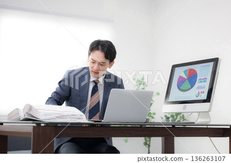 畫面中，一位身著西裝的男士，神情焦慮、心事重重、忙碌不堪、焦躁不安，他可能是位總裁或經理，正在查看一張業務戰略和業績圖表。 136263107