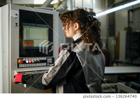 Woman operates machine in workshop during daytime Woman operates machine in workshop during daytime 136264740