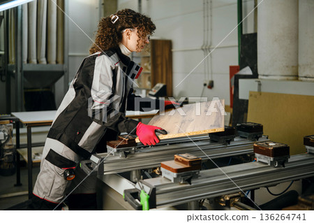 Woman works on wood in a carpentry workshop with tools and machinery in the background Woman works on wood in a carpentry workshop with tools and machinery in the background 136264741