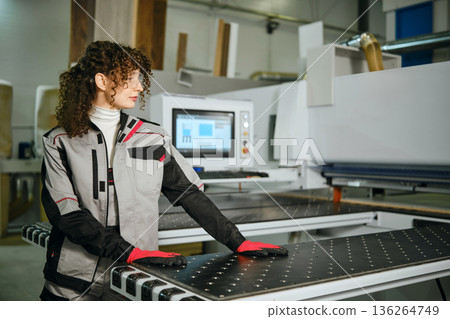 Woman works at wood cutting machine in a workshop during daytime in a modern setting Woman works at wood cutting machine in a workshop during daytime in a modern setting 136264749