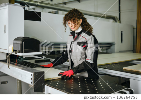 Woman works on CNC machine in factory during day while wearing gloves and safety gear Woman works on CNC machine in factory during day while wearing gloves and safety gear 136264753