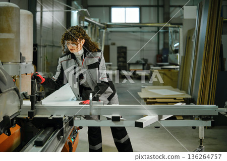Worker operates circular saw in a factory during a busy workday inside a workshop 136264757