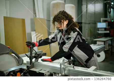 Woman works on cutting machine in a workshop during daytime in a manufacturing space 136264760