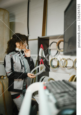 Woman examines metal rings in workshop while wearing work clothing and safety glasses Woman examines metal rings in workshop while wearing work clothing and safety glasses 136264765