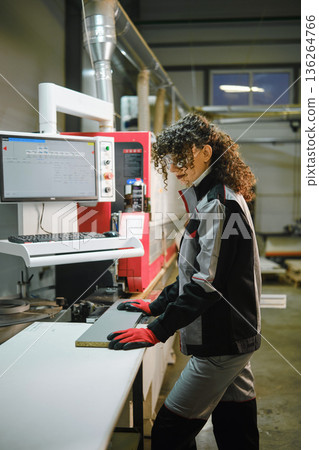 Worker uses equipment to cut material in a factory setting during daytime hours Worker uses equipment to cut material in a factory setting during daytime hours 136264766