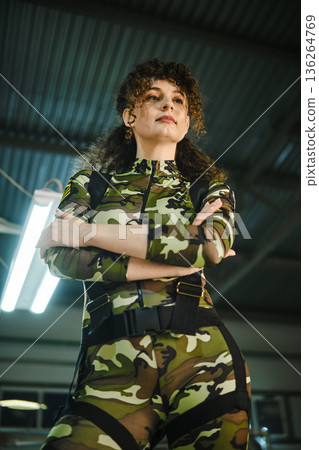 Woman in camouflage suit stands with arms crossed 136264769