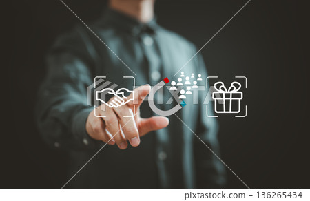 Businessman interacting with digital icons of handshake, magnet attracting people, and gift box illustrating customer engagement and loyalty 136265434