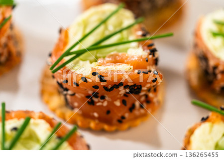 A close-up of a smoked salmon jumbo cream cheese roll, highlighting its intricate details. The roll features a creamy filling with cucumber slices wrapped in smoked salmon and coated in a mix of black A close-up of a smoked salmon jumbo cream cheese roll, highlighting its intricate details. The roll features a creamy filling with cucumber slices wrapped in smoked salmon and coated in a mix of black 136265455