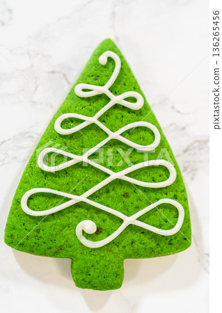 A close-up of a green Christmas tree cookie decorated with intricate white icing swirls and fine sugar crystal accents. A close-up of a green Christmas tree cookie decorated with intricate white icing swirls and fine sugar crystal accents. 136265456