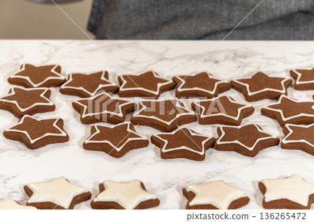 A batch of gingerbread star cookies in various stages of icing, showcasing the step-by-step process of decorating holiday treats with royal icing. A batch of gingerbread star cookies in various stages of icing, showcasing the step-by-step process of decorating holiday treats with royal icing. 136265472
