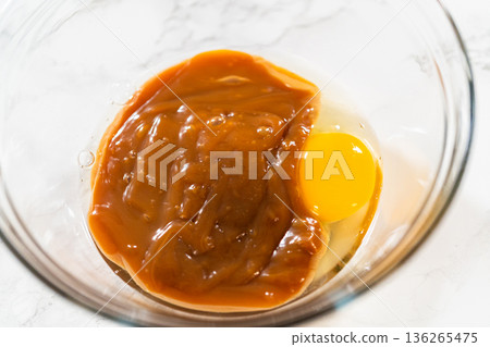 A glass bowl holds caramel sauce, an egg, and flour, ready to be whisked into a smooth, rich filling for the Gingerbread Bundt Cake With Caramel. A glass bowl holds caramel sauce, an egg, and flour, ready to be whisked into a smooth, rich filling for the Gingerbread Bundt Cake With Caramel. 136265475