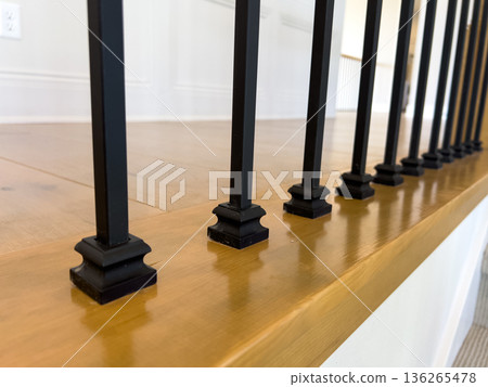Close-up of sleek black iron stair spindles mounted on glossy wooden trim above carpeted stairs. Perfect for illustrating home interiors or stair detail work. 136265478