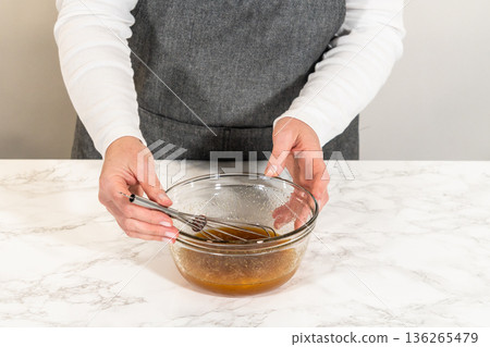 Front view of a small glass bowl with an egg and maple syrup, placed on a marble countertop, ready to be added to the Chocolate Ginger Sugar Cookie Dough mixture. 136265479