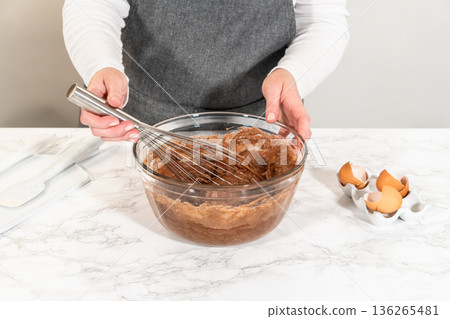 With a hand whisk, the ingredients are expertly mixed in a glass mixing bowl - creating this delectable Chocolate Bundt Cake. With a hand whisk, the ingredients are expertly mixed in a glass mixing bowl - creating this delectable Chocolate Bundt Cake. 136265481