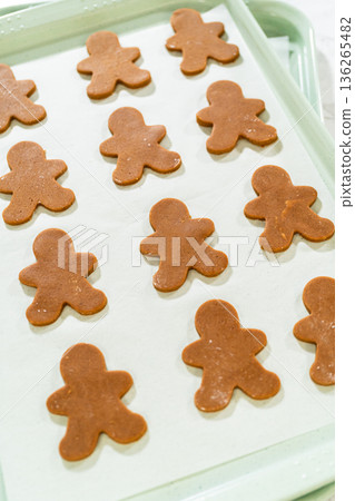 Angled view of unbaked gingerbread man cookies evenly arranged on a parchment-lined baking sheet. Angled view of unbaked gingerbread man cookies evenly arranged on a parchment-lined baking sheet. 136265482