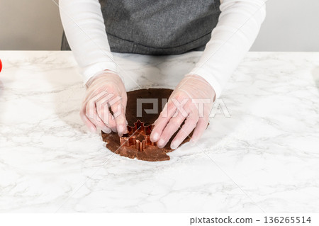 Overhead view of snowflake-shaped Chocolate Ginger Sugar Cookie dough being cut using a copper cookie cutter on a marble surface. Overhead view of snowflake-shaped Chocolate Ginger Sugar Cookie dough being cut using a copper cookie cutter on a marble surface. 136265514